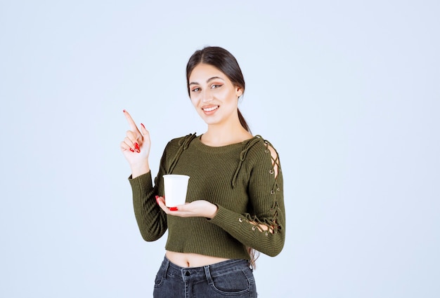 femme brune tenant une tasse en plastique et pointant quelque part.