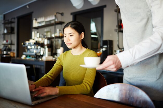 Femme buvant du café ou du thé en travaillant sur l'ordinateur portable