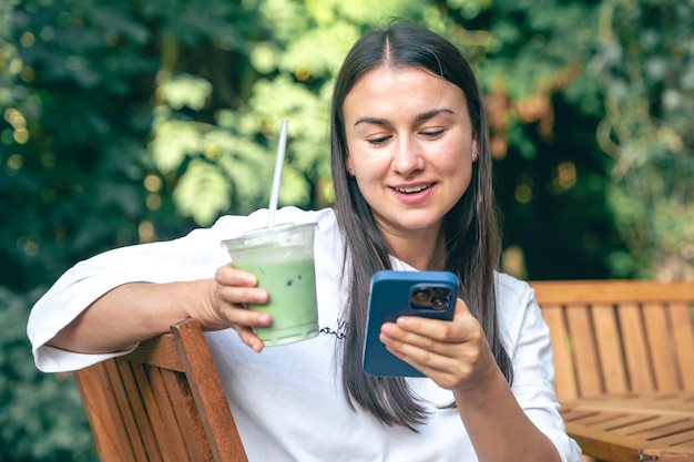 Photo gratuite une femme buvant du café matcha latte et utilisant un smartphone dans un café