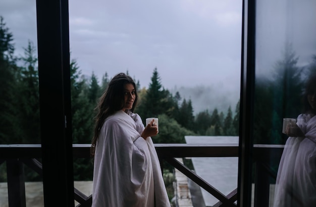 Photo gratuite femme buvant du thé sur un balcon confortable d'une maison de campagne