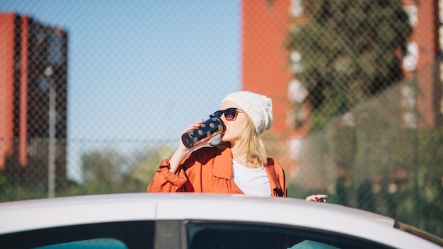 Femme buvant près de voiture