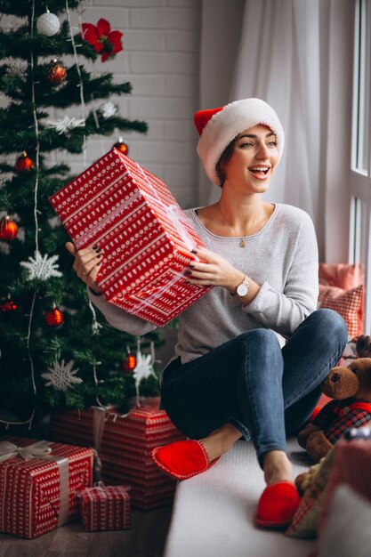 Femme avec des cadeaux de Noël par sapin de Noël