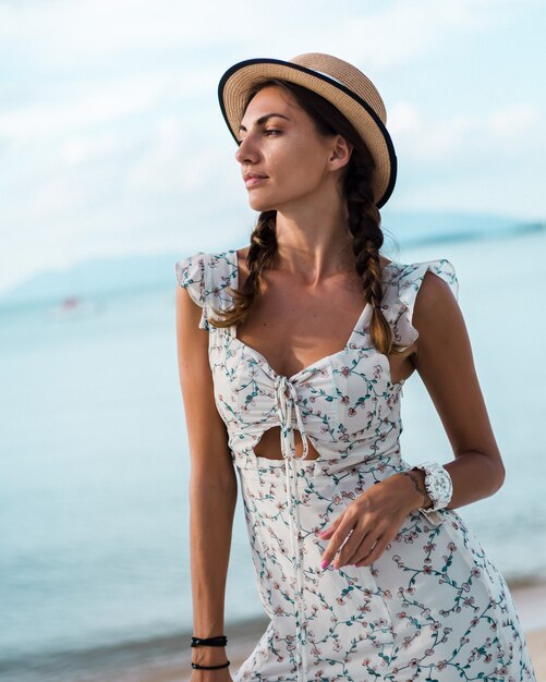 Femme calme positive en robe d'été légère, chapeau de paille, emplacement tropical