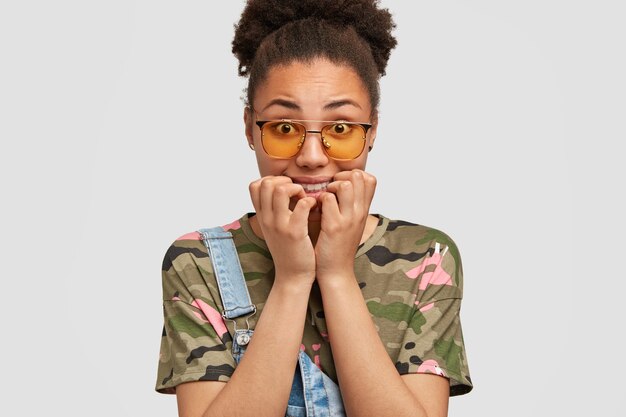 Femme de camouflage nerveux posant contre le mur blanc