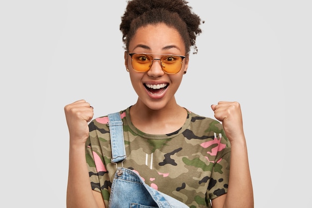 Femme de camouflage ravie posant contre le mur blanc