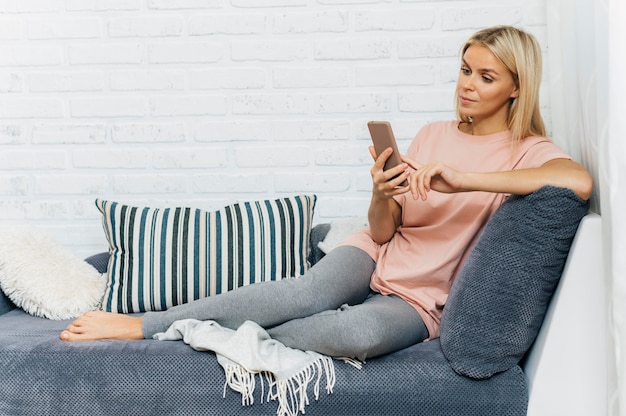 Femme sur le canapé à l'aide de smartphone à la maison pendant la pandémie