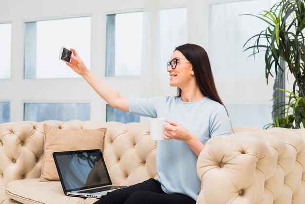 Femme sur un canapé prenant selfie avec café