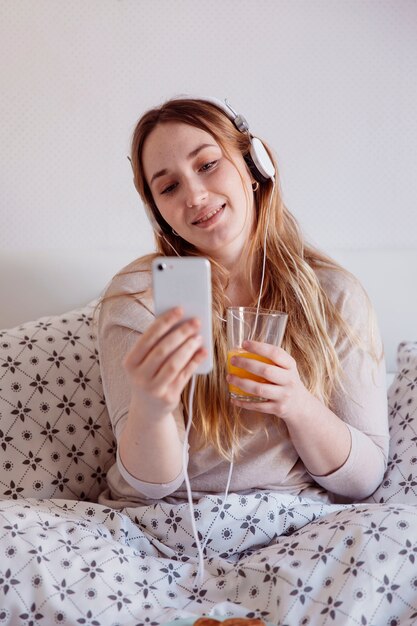 Femme avec casque et jus en utilisant un smartphone