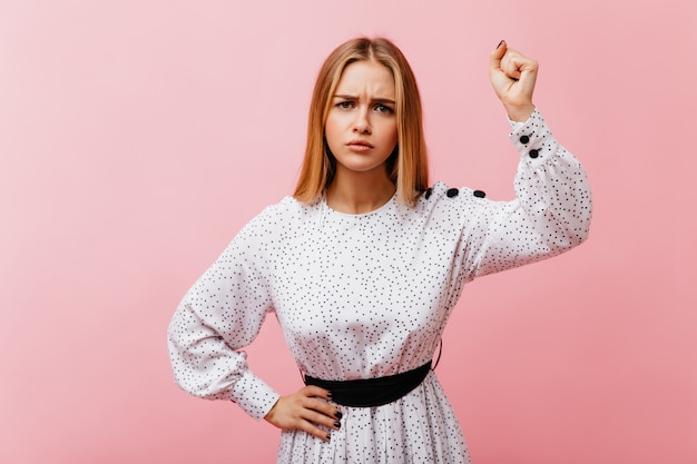 Femme caucasienne bouleversée en chemise à la mode posant. Debonair slim femme en chemisier blanc debout sur rose.