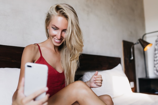 Femme caucasienne bronzée insouciante à l'aide de téléphone pour selfie. Jolie femme riante avec une peau bronzée prenant une photo d'elle-même.