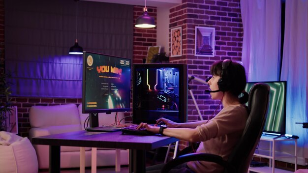 Femme caucasienne célébrant la première place dans la compétition multijoueur en ligne de jeu d'action depuis chez elle. Gamer girl jouant à la simulation de tireur spatial sur une configuration pc professionnelle avec clavier de jeu.