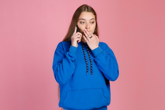 Photo gratuite une femme caucasienne choquée étonnée couvrant la bouche avec la main tout en parlant au téléphone à l'intérieur