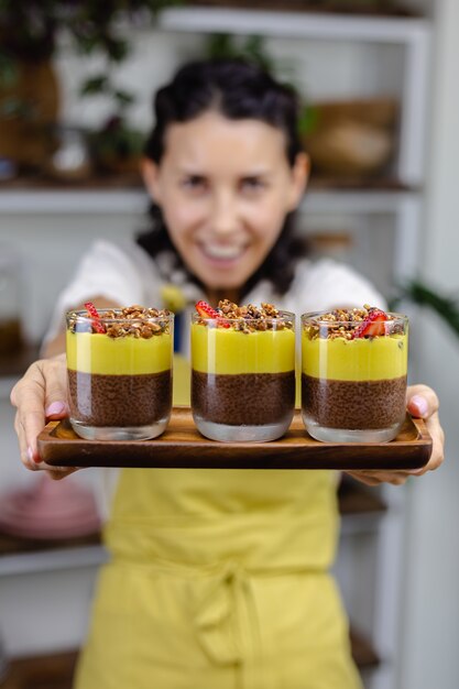 Femme caucasienne dans la cuisine fait des puddings de chia avec de la confiture de mangue. Désert fait de lait d'amande, graines de chia, cacao, confiture de mangue et granola.