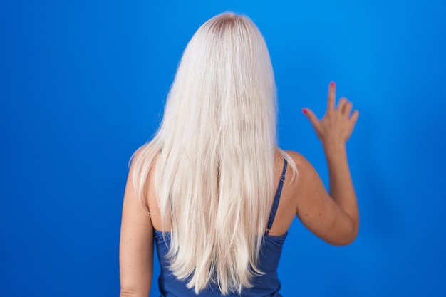 Photo gratuite femme caucasienne debout sur fond bleu posant en arrière pointant vers l'avant avec la main du doigt