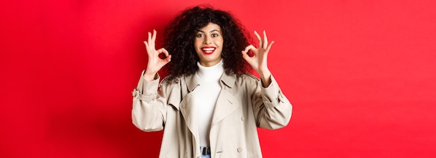 Femme caucasienne élégante en trench-coat montrant un geste correct et souriant satisfait recommandant compa