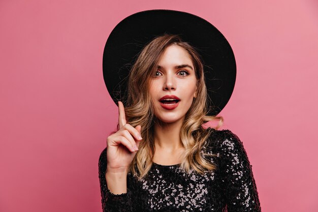 Femme caucasienne intéressée aux cheveux bruns posant Superbe dame bien habillée debout sur un mur rose.