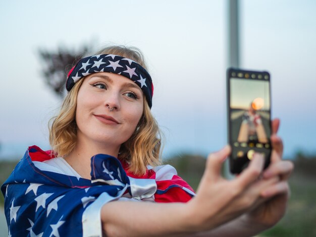 Femme caucasienne patriotique prenant un selfie avec le drapeau américain drapé autour d'elle
