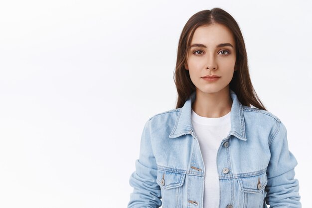 Femme caucasienne sournoise et méfiante en gros plan, loucher avec un air douteux sceptique, avoir de l'incrédulité dans vos paroles, debout incertaine et hésitante sur fond blanc, porter une veste en jean sur un t-shirt