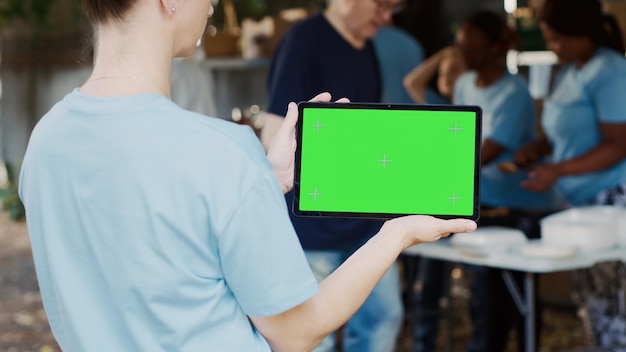 Photo gratuite une femme caucasienne tenant horizontalement une tablette numérique avec un écran vert chromakey dans une banque alimentaire en plein air un appareil intelligent affichant un modèle de maquette vide tenu par une travailleuse caritative en plein air