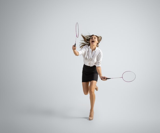 Une femme caucasienne en tenue de bureau joue au badminton isolé sur un mur gris