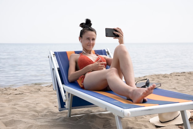 Femme sur une chaise de plage prenant un selfie