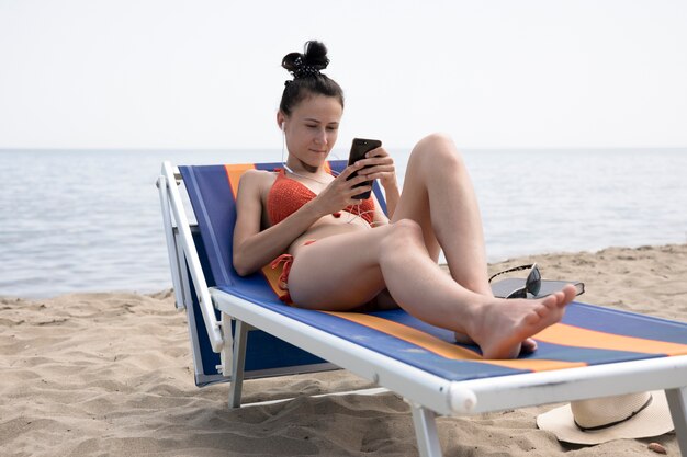 Femme, chaise plage, regarder téléphone