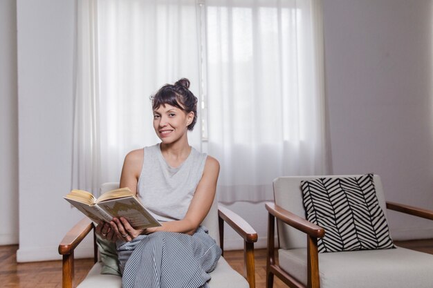 Femme en chaise en train de lire un livre et souriant