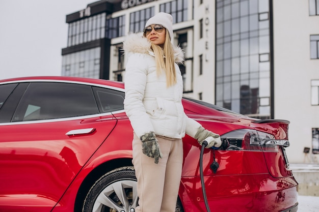 Femme chargeant une voiture électrique rouge, en hiver