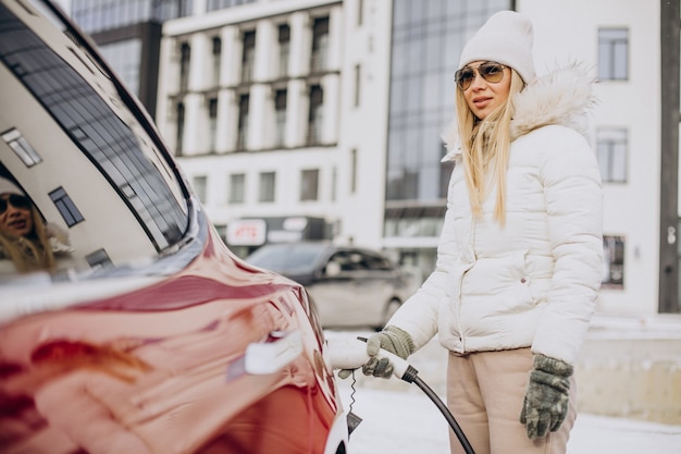 Femme chargeant une voiture électrique rouge, en hiver