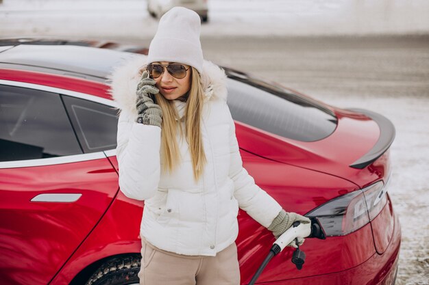 Femme chargeant une voiture électrique rouge, en hiver