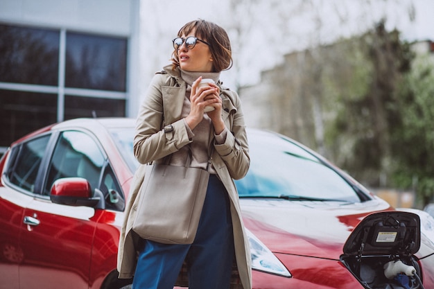 Femme chargeant une voiture électrique à la station d&#39;essence électrique et buvant du café