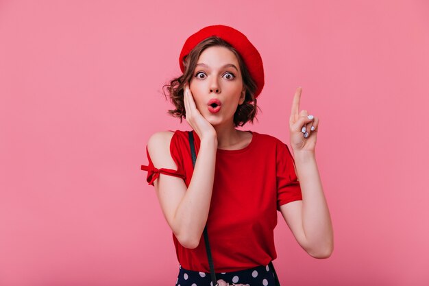 Femme charmante choquée dans l'élégant béret posant. Portrait intérieur de jolie dame caucasienne en tenue française.