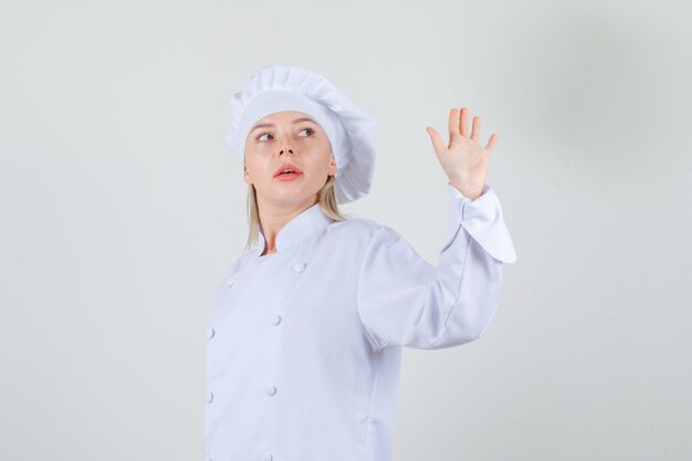 Femme chef agitant la main tout en regardant en arrière en uniforme blanc.