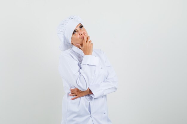 Femme chef debout dans la pensée pose en uniforme blanc et à la recherche de rêve