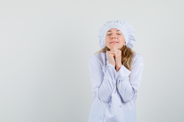 Femme chef joignant les mains en geste de prière en uniforme blanc et à la recherche d'espoir.