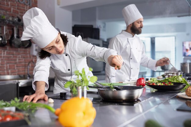 Une femme chef perfectionne un repas gourmet en ajoutant des herbes fraîches dans la cuisine