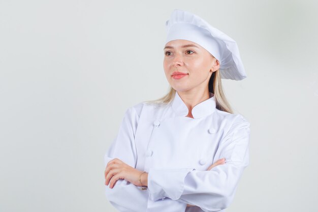 Femme chef à la recherche de côté avec les bras croisés en uniforme blanc et à la bonne humeur.