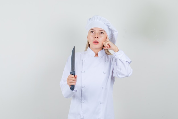 Femme chef tenant un couteau et pensant en uniforme blanc