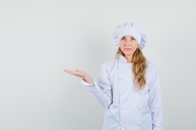 Femme chef tenant la paume comme montrant quelque chose en uniforme blanc