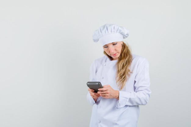 Femme chef en uniforme blanc faisant des calculs sur la calculatrice