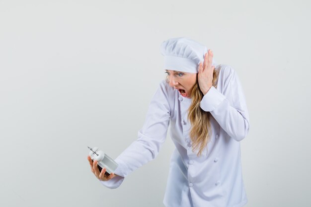 Femme chef en uniforme blanc regardant réveil et à l'agitation