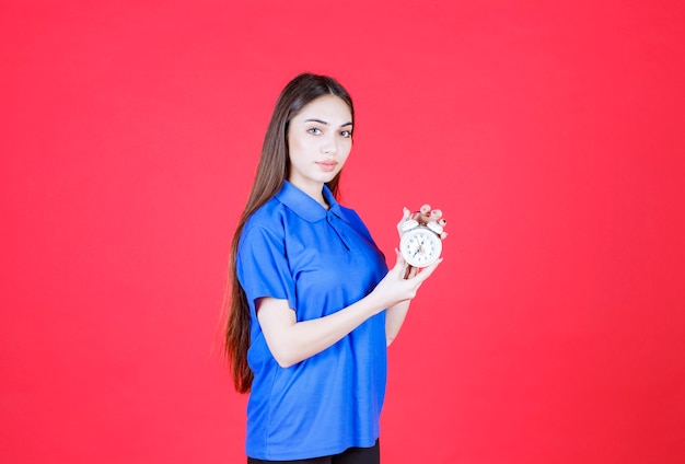 femme en chemise bleue tenant un réveil.