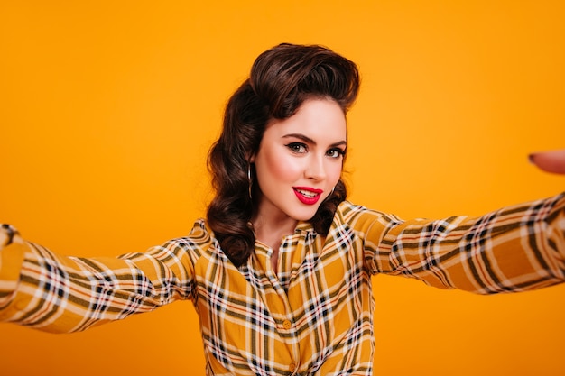 Photo gratuite femme en chemise à carreaux prenant selfie. photo de studio de pin-up souriant posant sur fond jaune.