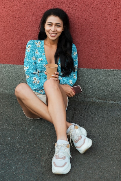 Femme avec une chemise à fleurs assis et tenant son téléphone