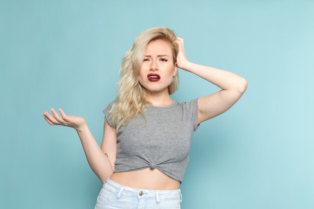 Femme en chemise grise et jeans bleu vif posant avec une expression confuse