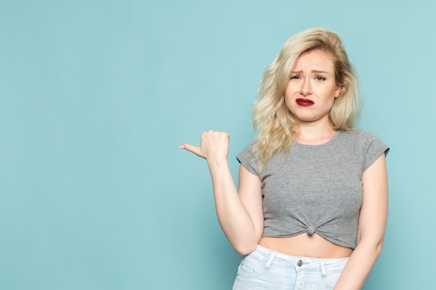 Femme en chemise grise et jeans bleu vif posant avec une expression mécontente