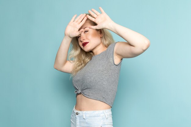 Femme en chemise grise et jeans bleu vif posant avec une expression prudente