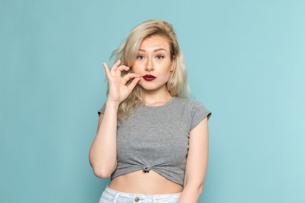 Femme en chemise grise et jeans bleu vif posant avec une expression silencieuse