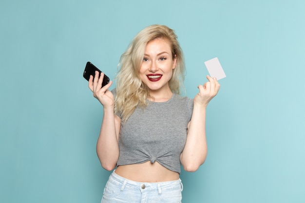 Femme en chemise grise et jeans bleu vif tenant le téléphone et la carte blanche