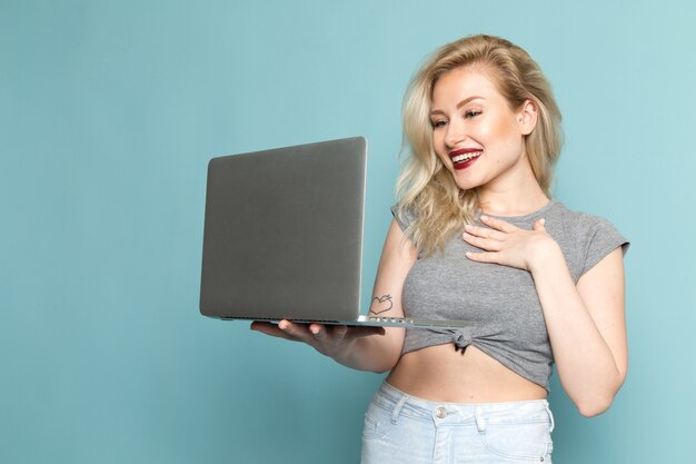 Femme en chemise grise et jeans bleu vif utilisant un ordinateur portable